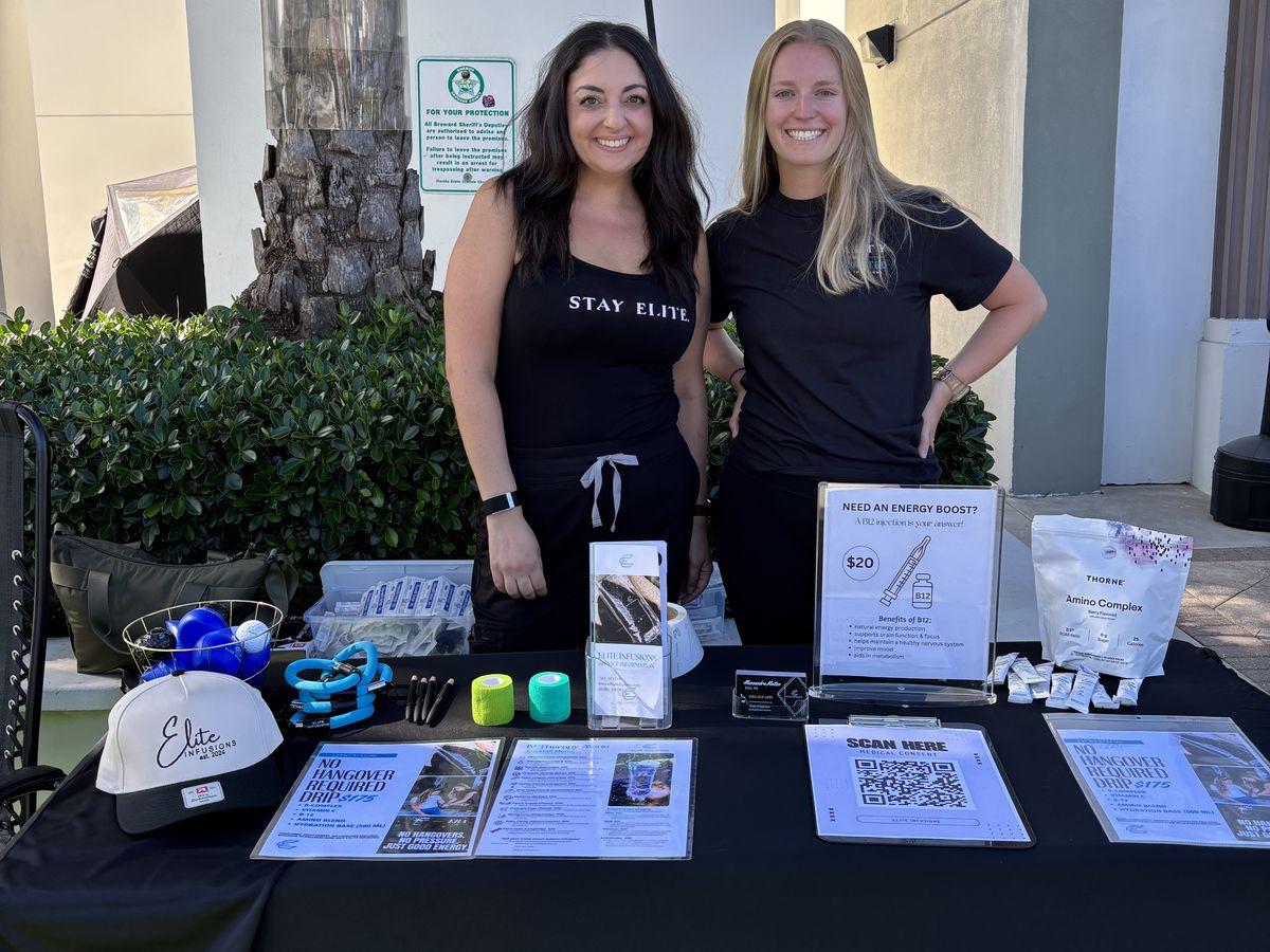 Two Elite nurses smiling behind a branded wellness pop-up table