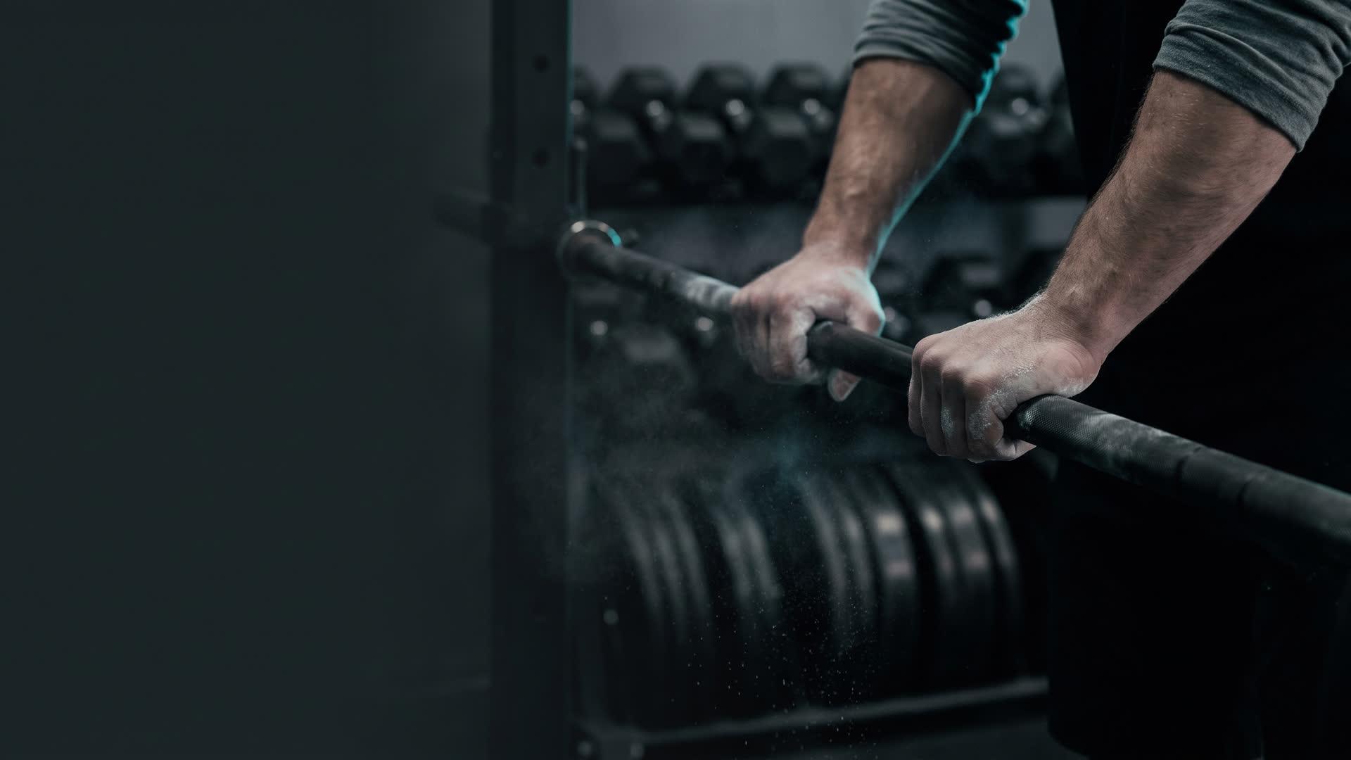 An athlete's chalked hands gripping a barbell in a dark gym